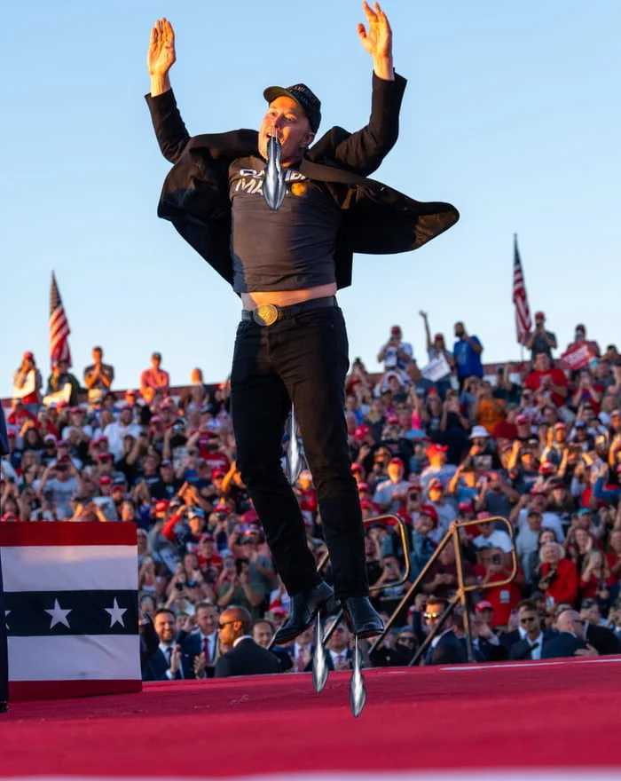 Man in black outfit jumping with arms raised in victory pose before…
