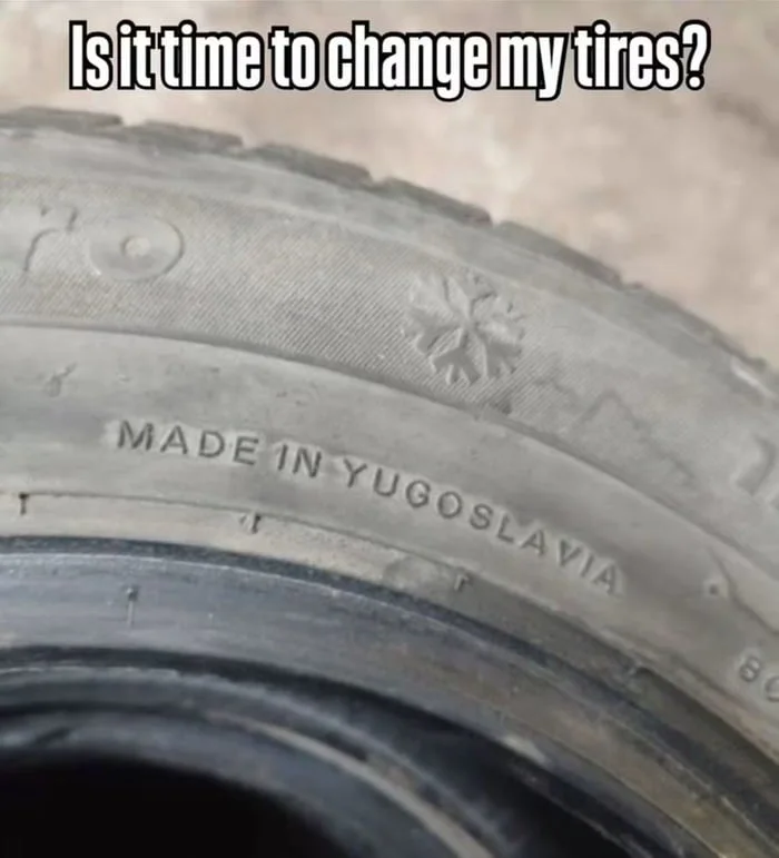 A Balkan thing. Worn tire with tread worn down to snowflake symbols, marked as made in Yugoslavia, humorously suggesting it needs replacement. Text: Is it time to change my tires? / MADE IN YUGOSLAVIA