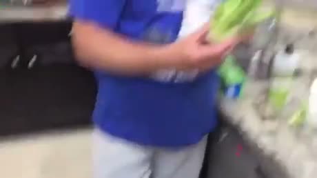 Person in blue shirt holding green items near shelving, appears to…