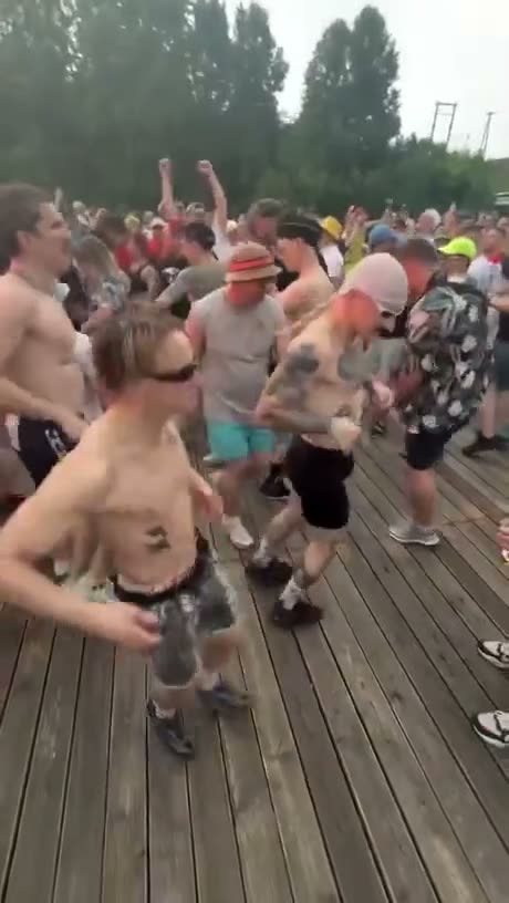 Large crowd of people dancing and celebrating on a wooden deck…