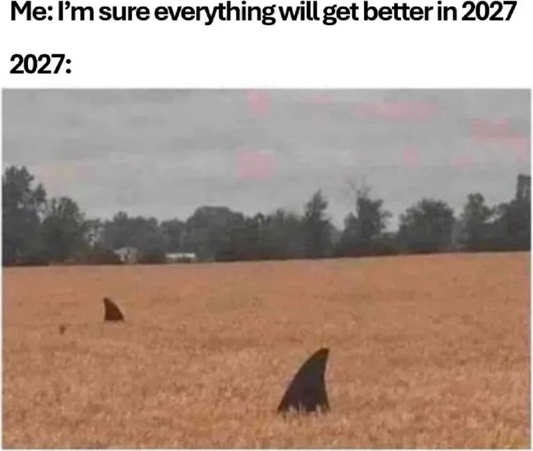 My optimism meets reality. A desert landscape with shark fins protruding from sand, suggesting apocalyptic conditions. Text: Me: I'm sure everything will get better in 2027 / 2027: