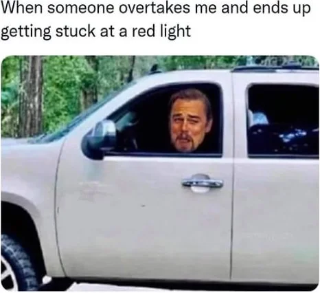 Man in white truck looking satisfied while stopped at red light after being overtaken by another vehicle. Text: When someone overtakes me and ends up getting stuck at a red light