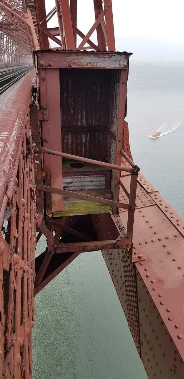Railway bridge lavatory. Rusty metal structural element on a bridge overlooking water with a boat visible below