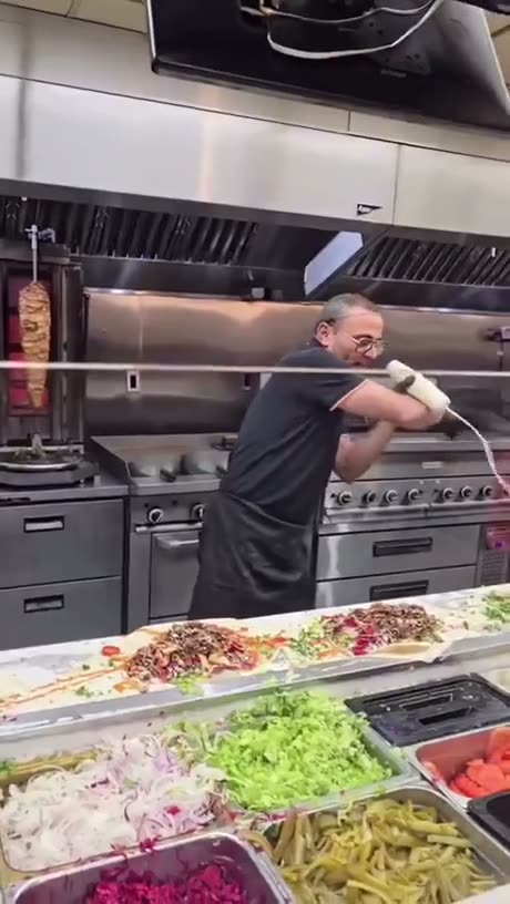 A man in a black shirt works at a commercial kitchen counter with…
