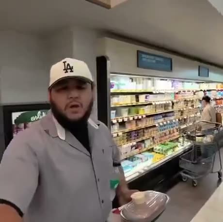 Man in LA cap and gray jacket standing in grocery store dairy…