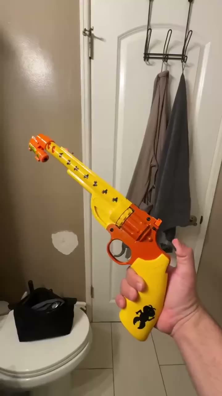 Person holding a large yellow and orange toy revolver in a bathroom.