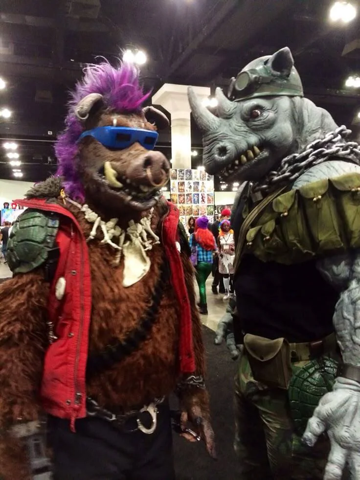 bebop and rocksteady. Two elaborate creature cosplayers at a convention, one with purple hair and blue visor, the other with horns and military gear