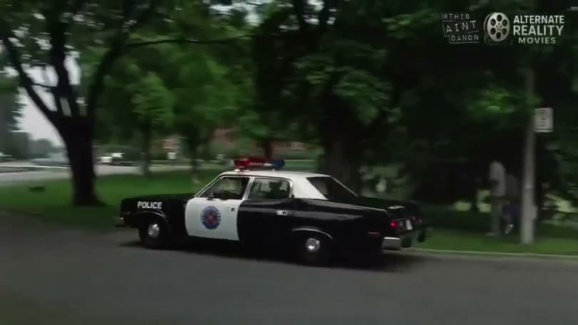 A classic police car drives down a tree-lined residential street in…