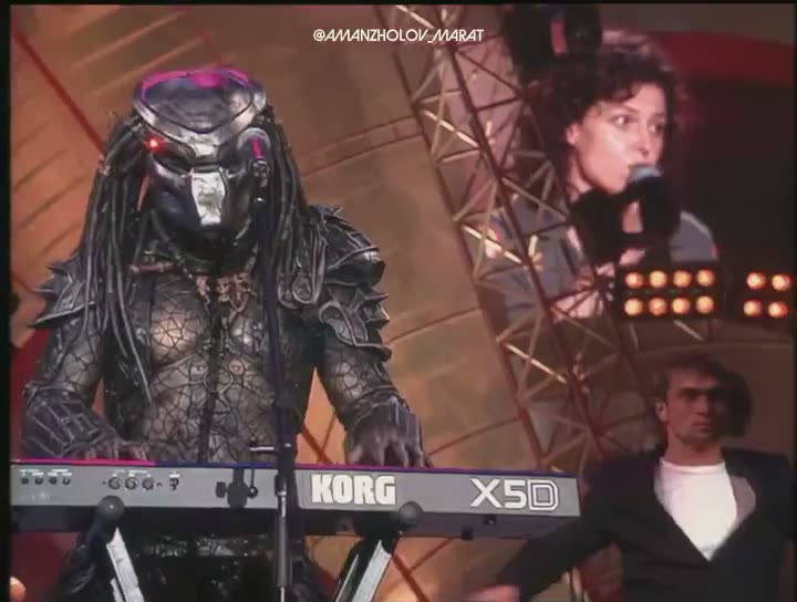 A person in an elaborate alien predator costume plays a Korg X50…