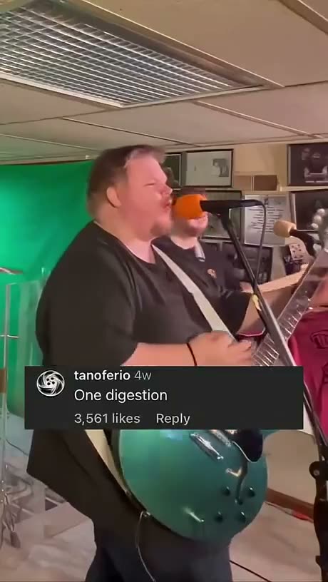 Two men singing into microphones in a studio setting with a green…