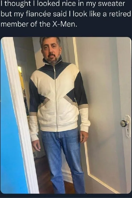 Man wearing a black and white color-blocked zip-up sweater with jeans, posing in a doorway. Text: I thought I looked nice in my sweater but my fiancée said I look like a retired member of the X-Men