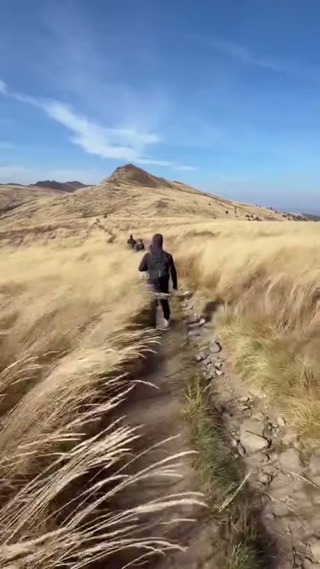 Hiker walking through grassy hillside terrain toward a distant…