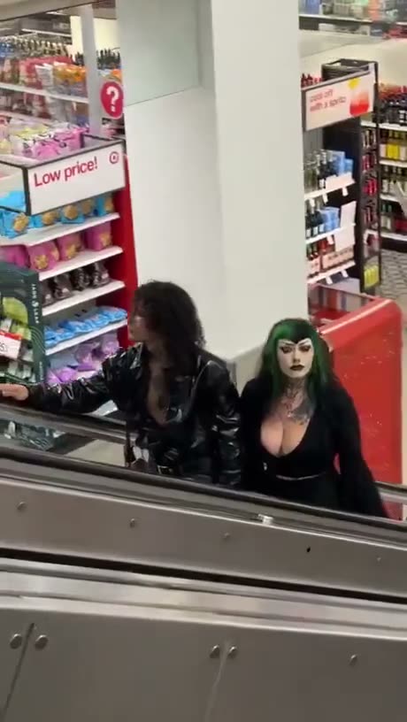 Two people in dark clothing with gothic makeup in a store aisle near…
