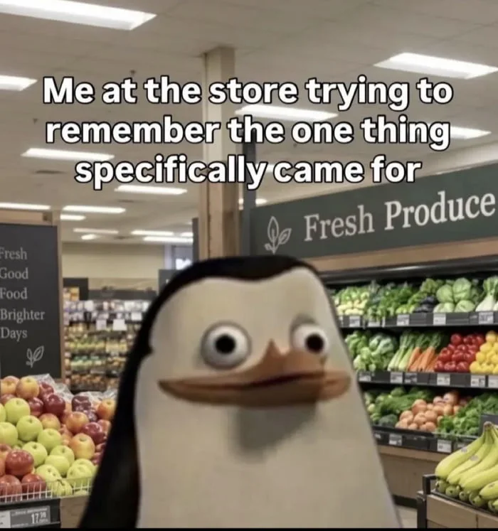A confused penguin character in a grocery store produce section with a bewildered expression. Text: Me at the store trying to remember the one thing specifically came for / Fresh Produce