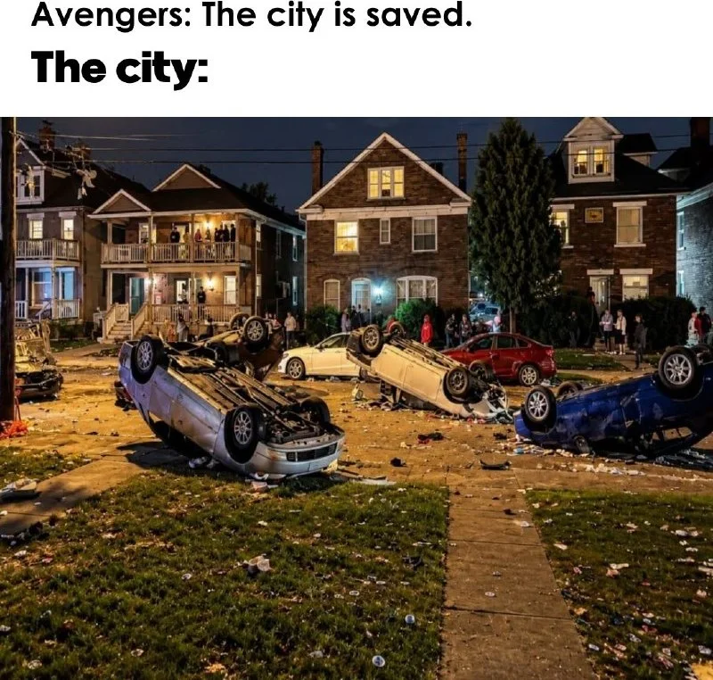 A residential neighborhood street filled with multiple overturned and destroyed cars at night. Text: Avengers: The city is saved. / The city: