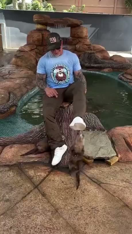 Man posing with an otter at a wildlife facility while wearing a New…