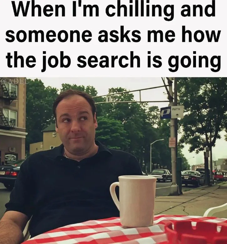 Job search progress report. Man sitting at outdoor table with coffee cup, making an uncomfortable facial expression. Text: When I'm chilling and someone asks me how the job search is going