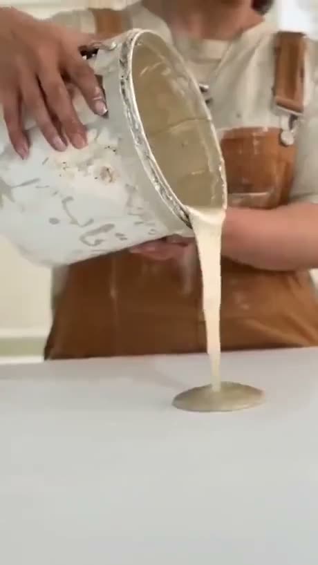 Person pouring a creamy liquid from a container onto a white surface…