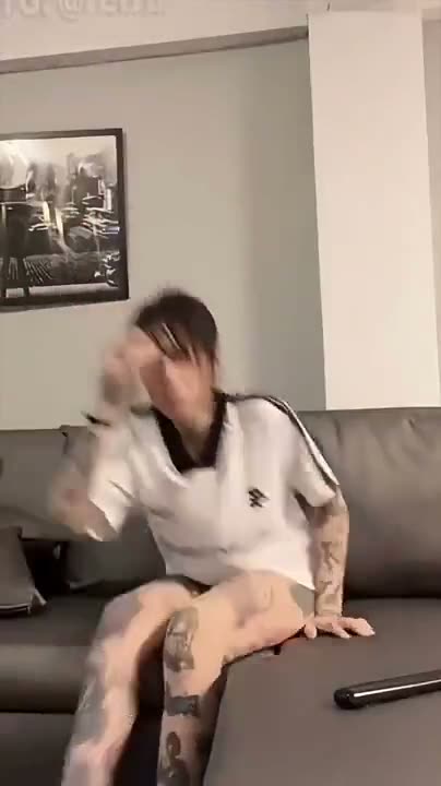 Person sitting on couch in casual white shirt with tattoos visible…