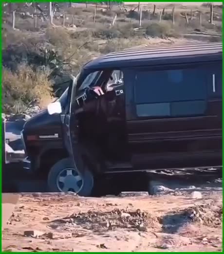 Dark van parked on sandy terrain with person visible in driver's…